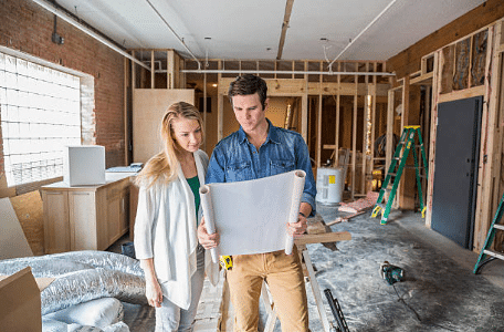 un homme et une femme dans une maison en construction qui regardent les plans